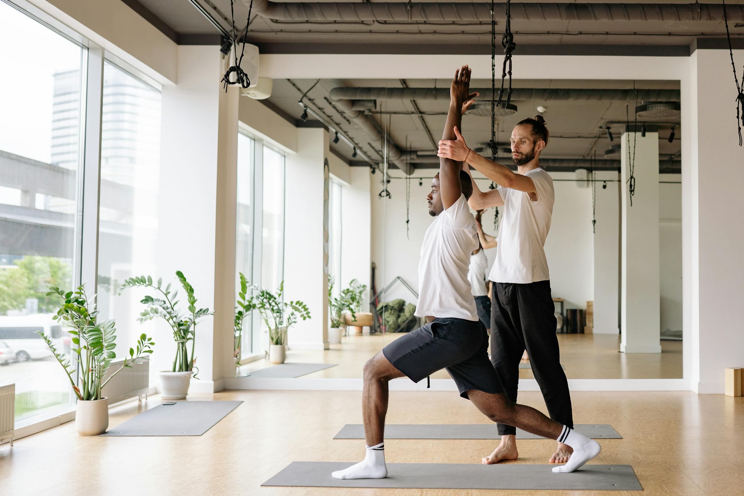 Instructor guides student in yoga pose in bright, modern studio.